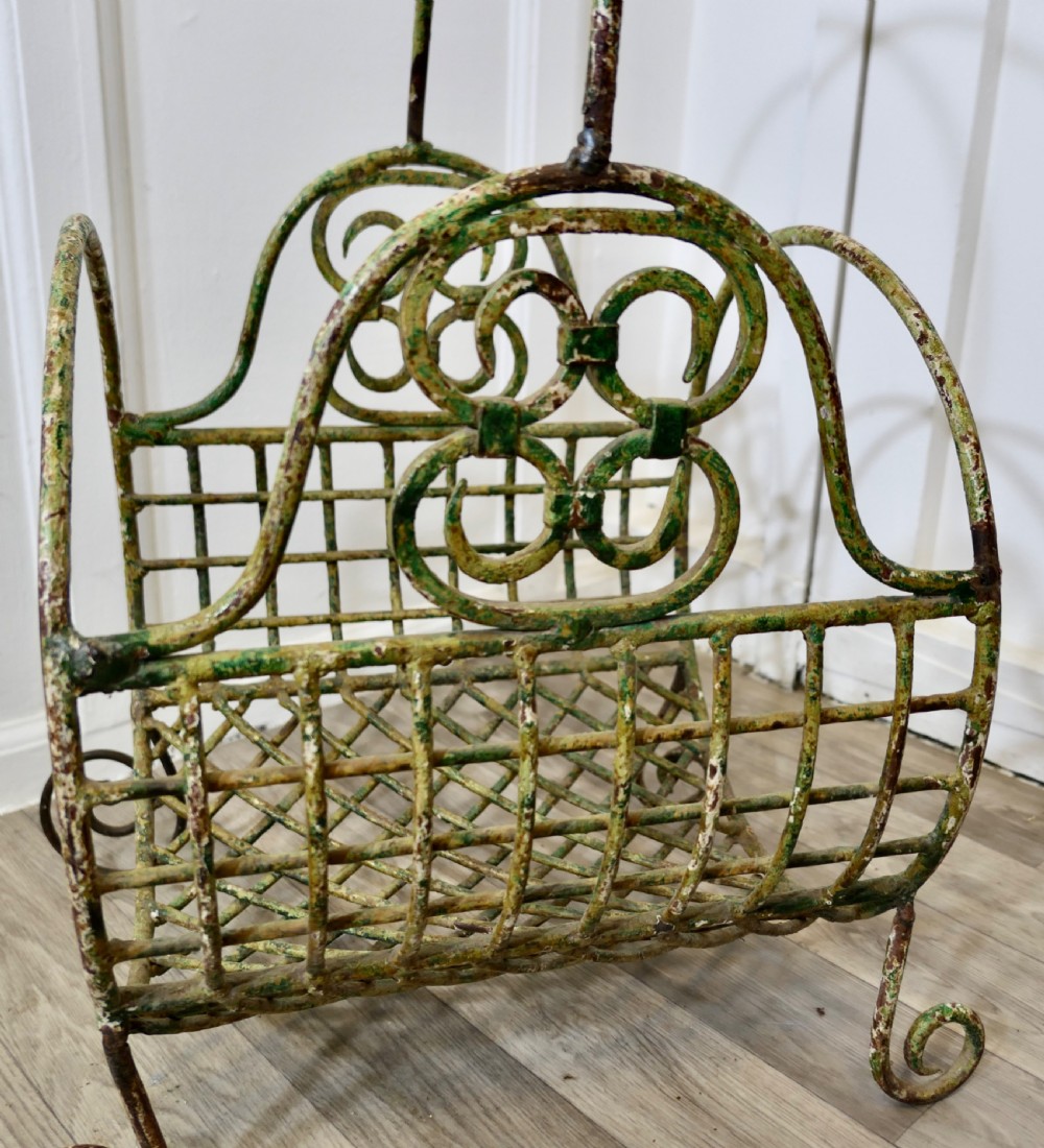 A 19th-century French distressed green painted wrought iron wirework log carrier featuring scroll feet, an elevated loop handle, and open mesh grid sides. View V