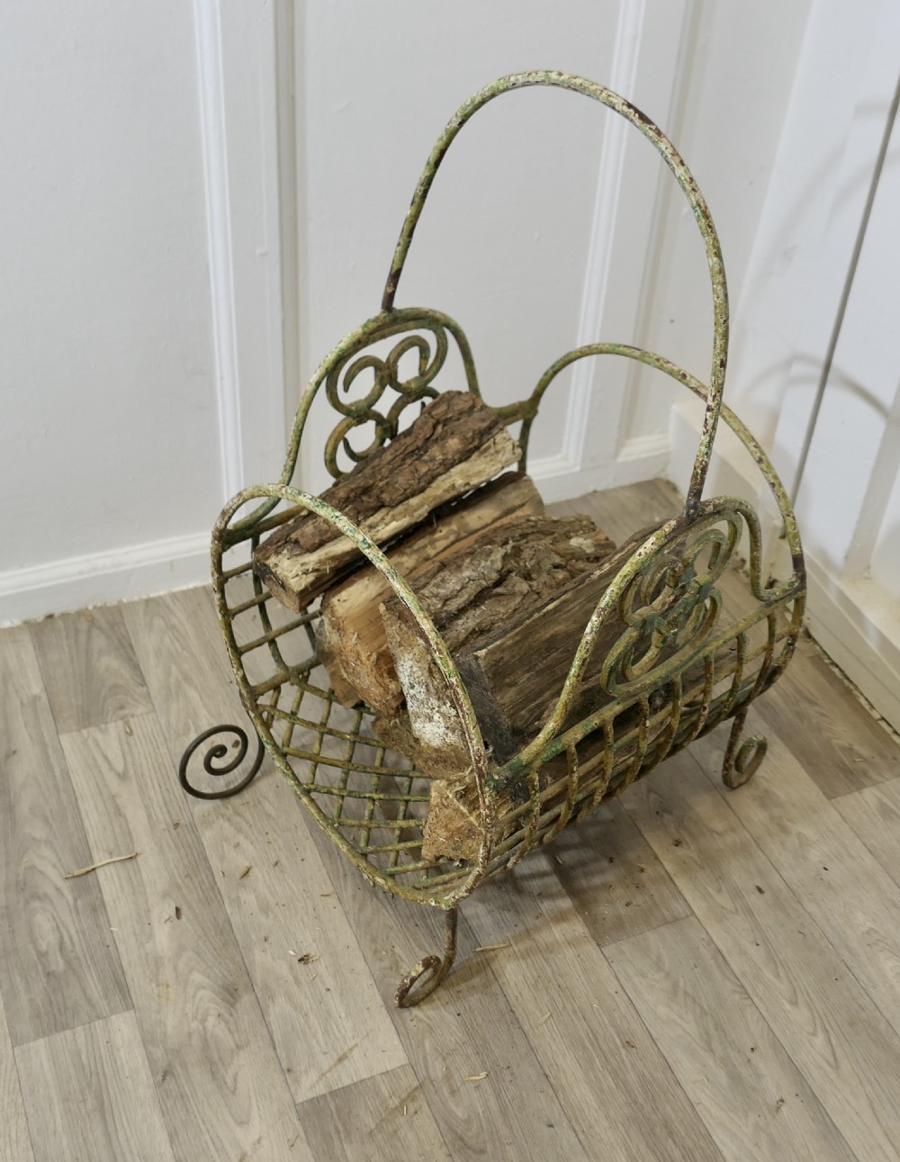 A 19th-century French distressed green painted wrought iron wirework log carrier featuring scroll feet, an elevated loop handle, and open mesh grid sides. View VIII