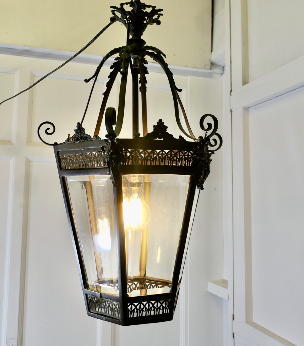 A dark patinated copper hexagonal ceiling lantern with glazed glass panels, scrolled metal supports, and cast Green Man mask decorations. View II
