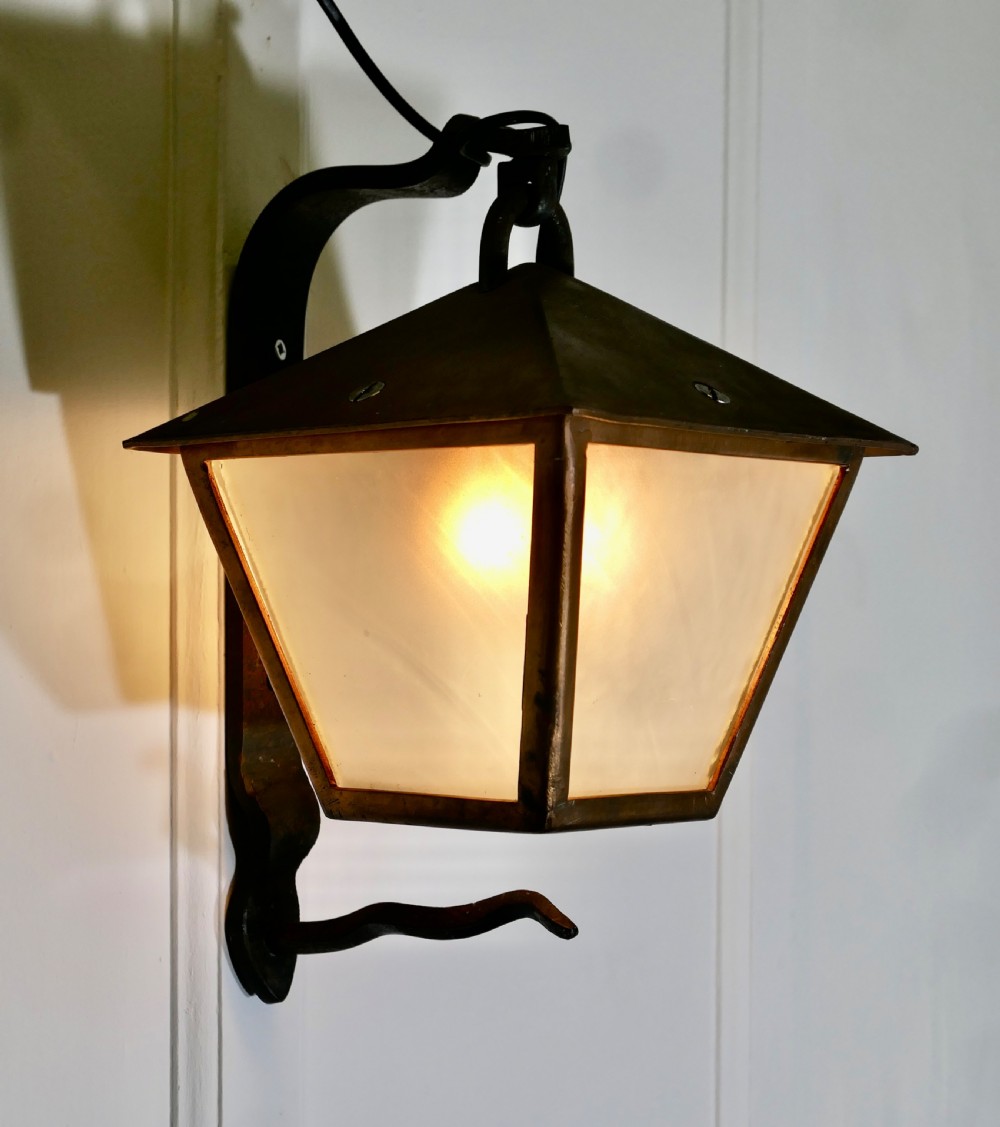 A wrought iron and copper wall lantern featuring a gooseneck bracket and frosted glass panels illuminated from within.