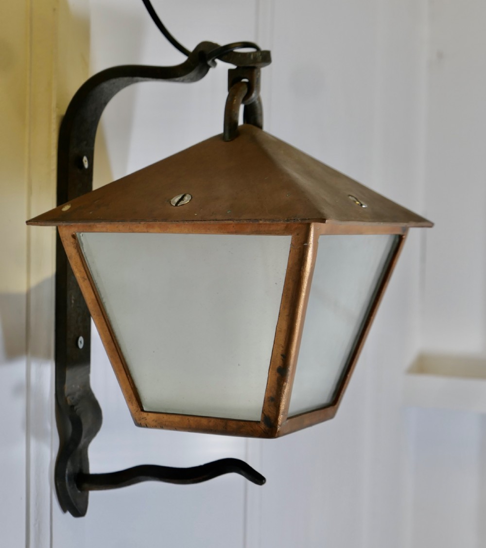 A wrought iron and copper wall lantern featuring a gooseneck bracket and frosted glass panels illuminated from within. View II
