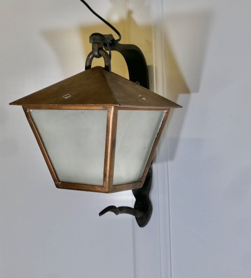 A wrought iron and copper wall lantern featuring a gooseneck bracket and frosted glass panels illuminated from within. View III