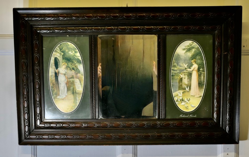 An Edwardian dark wood rectangular frame featuring a central rectangular mirror flanked by two oval colour prints depicting romantic figures. View VII