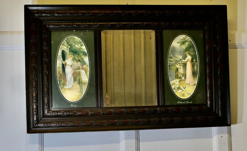 An Edwardian dark wood rectangular frame featuring a central rectangular mirror flanked by two oval colour prints depicting romantic figures. View II