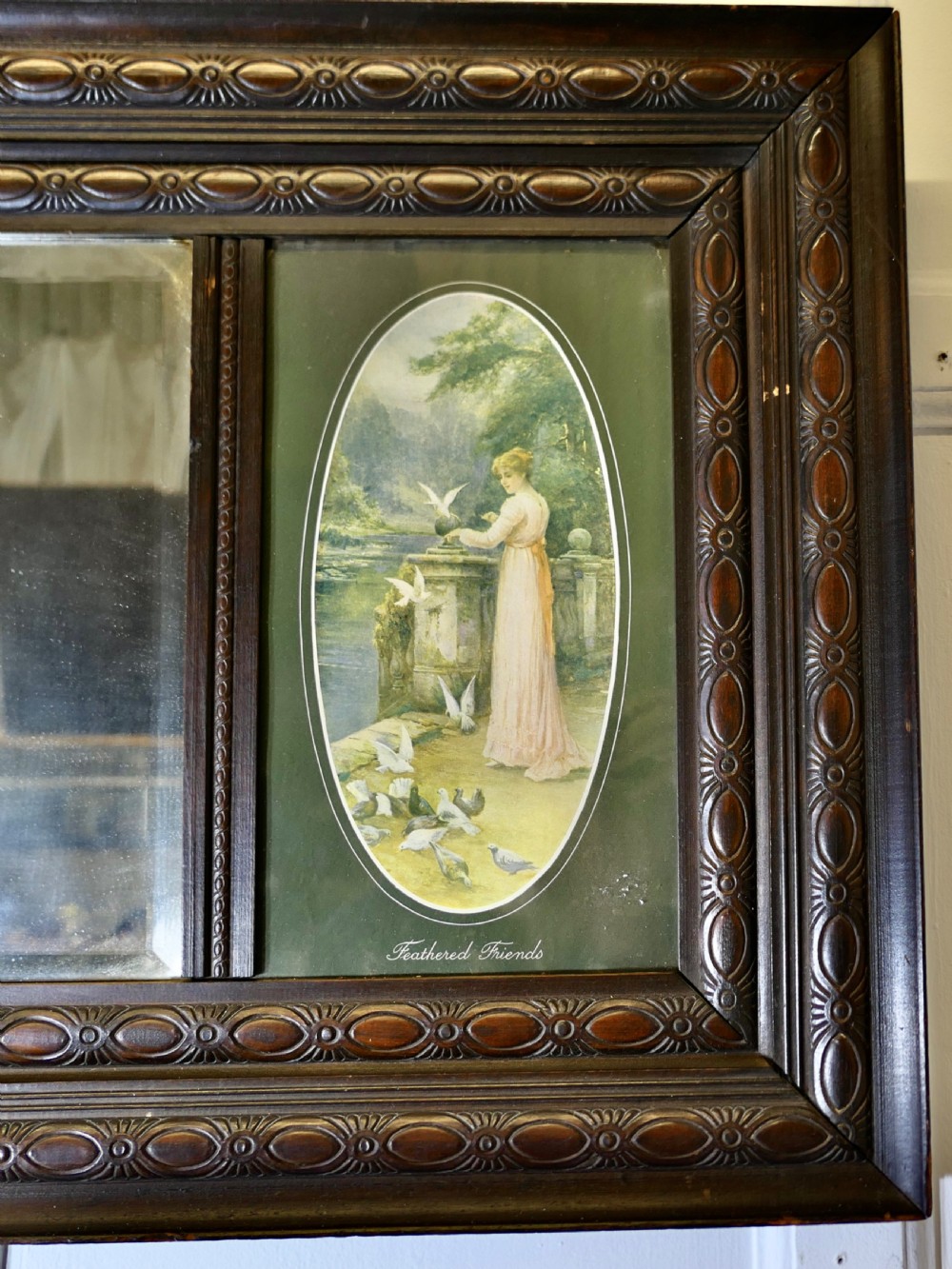 An Edwardian dark wood rectangular frame featuring a central rectangular mirror flanked by two oval colour prints depicting romantic figures. View V