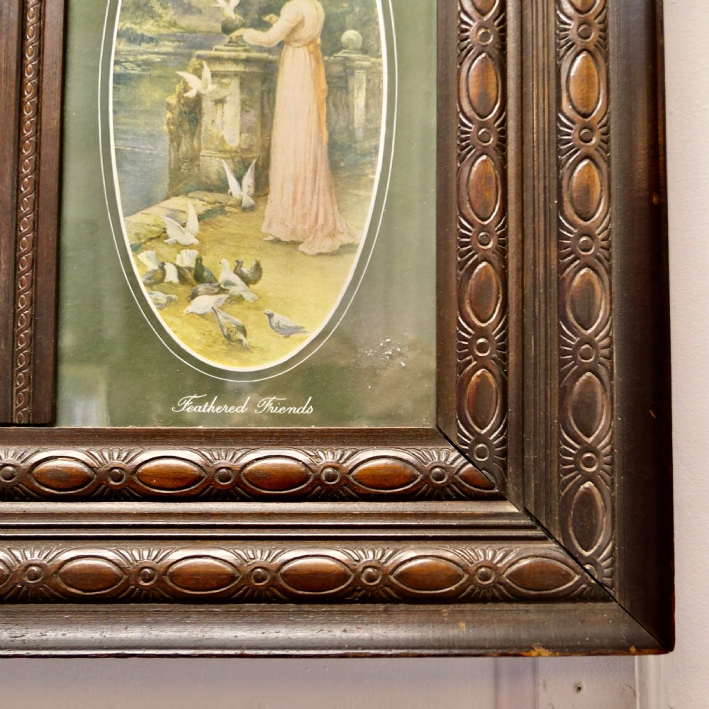 An Edwardian dark wood rectangular frame featuring a central rectangular mirror flanked by two oval colour prints depicting romantic figures. View VI