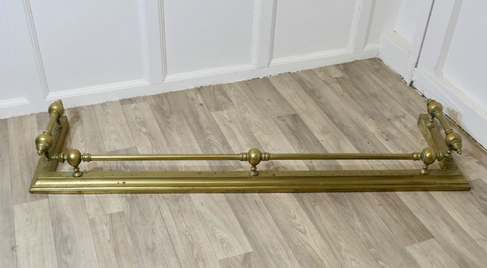 A large Victorian brass fireplace fender featuring a low moulded base topped with turned brass finials supporting a horizontal rail. View II