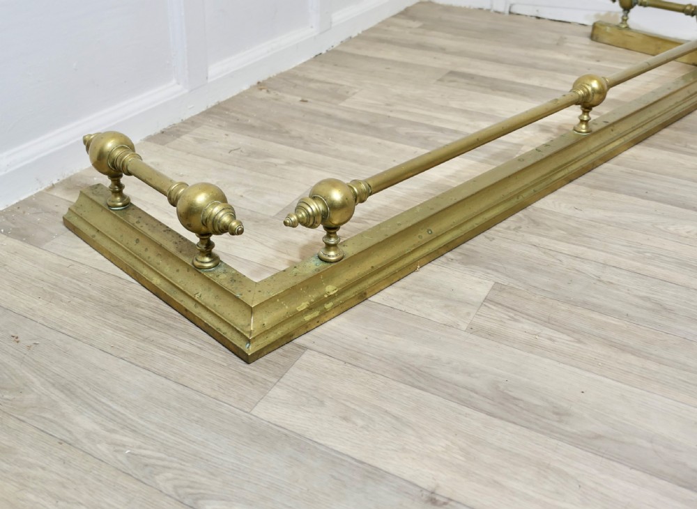 A large Victorian brass fireplace fender featuring a low moulded base topped with turned brass finials supporting a horizontal rail. View III
