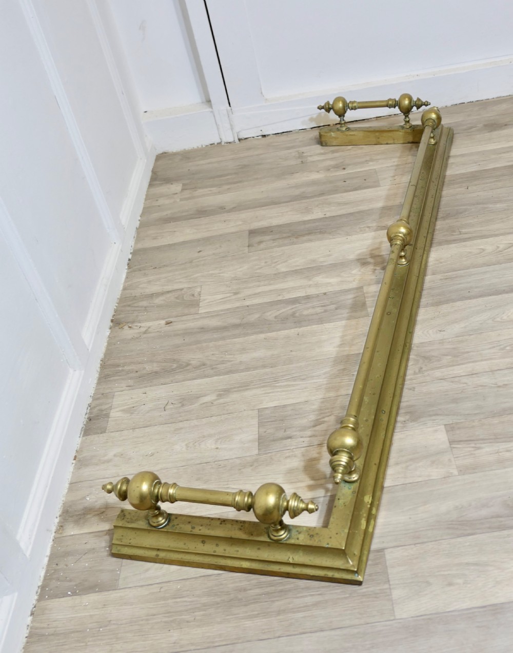 A large Victorian brass fireplace fender featuring a low moulded base topped with turned brass finials supporting a horizontal rail. View IV