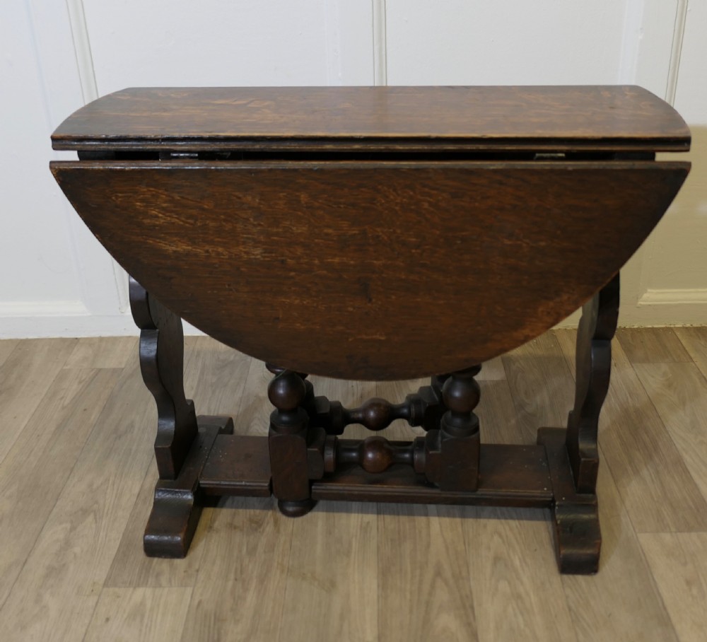 A dark oak low occasional coffee table with two drop-leaf flaps, turned bobbin legs, and a stretcher base.
