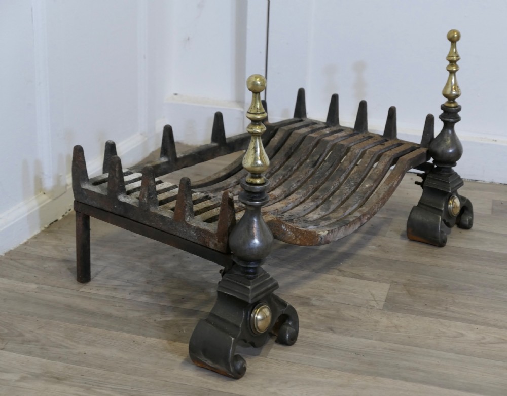 A heavy curved steel log grate supported by two front andirons featuring scroll feet, central brass cabochons, and turned brass urn finials. View VI