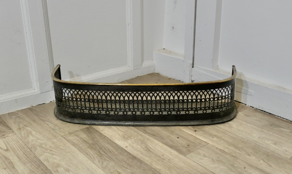 A Victorian curved fireplace fender featuring black pierced lattice ironwork topped with a polished brass rim.