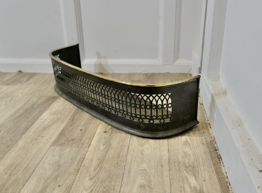 A Victorian curved fireplace fender featuring black pierced lattice ironwork topped with a polished brass rim. View II
