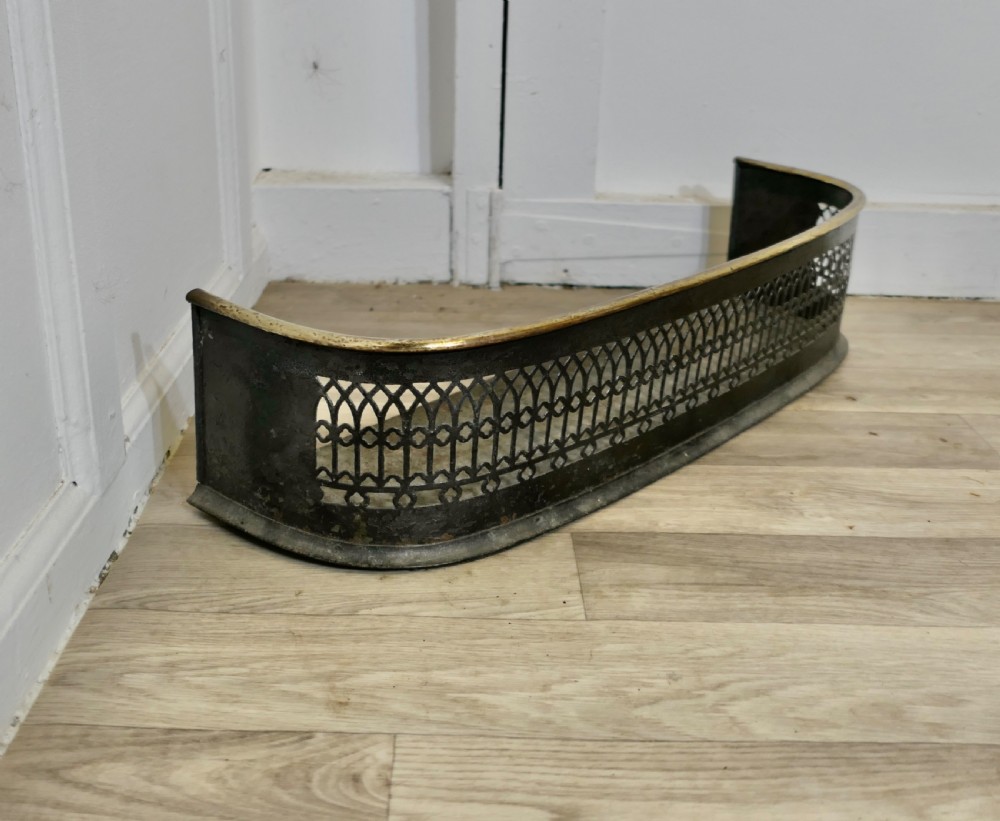A Victorian curved fireplace fender featuring black pierced lattice ironwork topped with a polished brass rim. View V