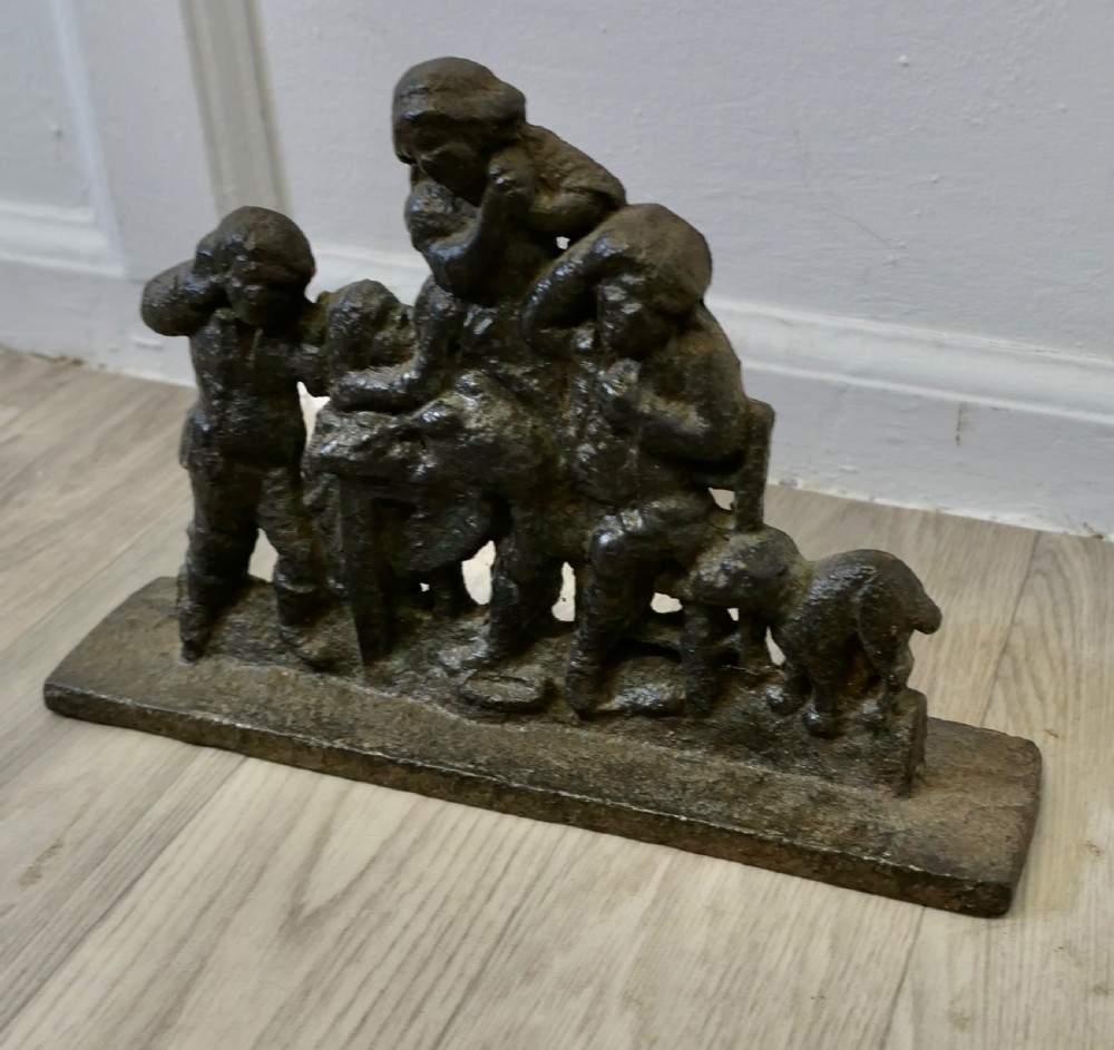 A 19th-century dark cast iron doorstop featuring a figurative narrative scene mounted on a flat rectangular plinth base. View II
