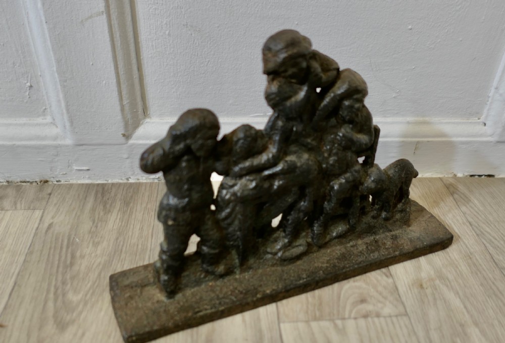 A 19th-century dark cast iron doorstop featuring a figurative narrative scene mounted on a flat rectangular plinth base. View V
