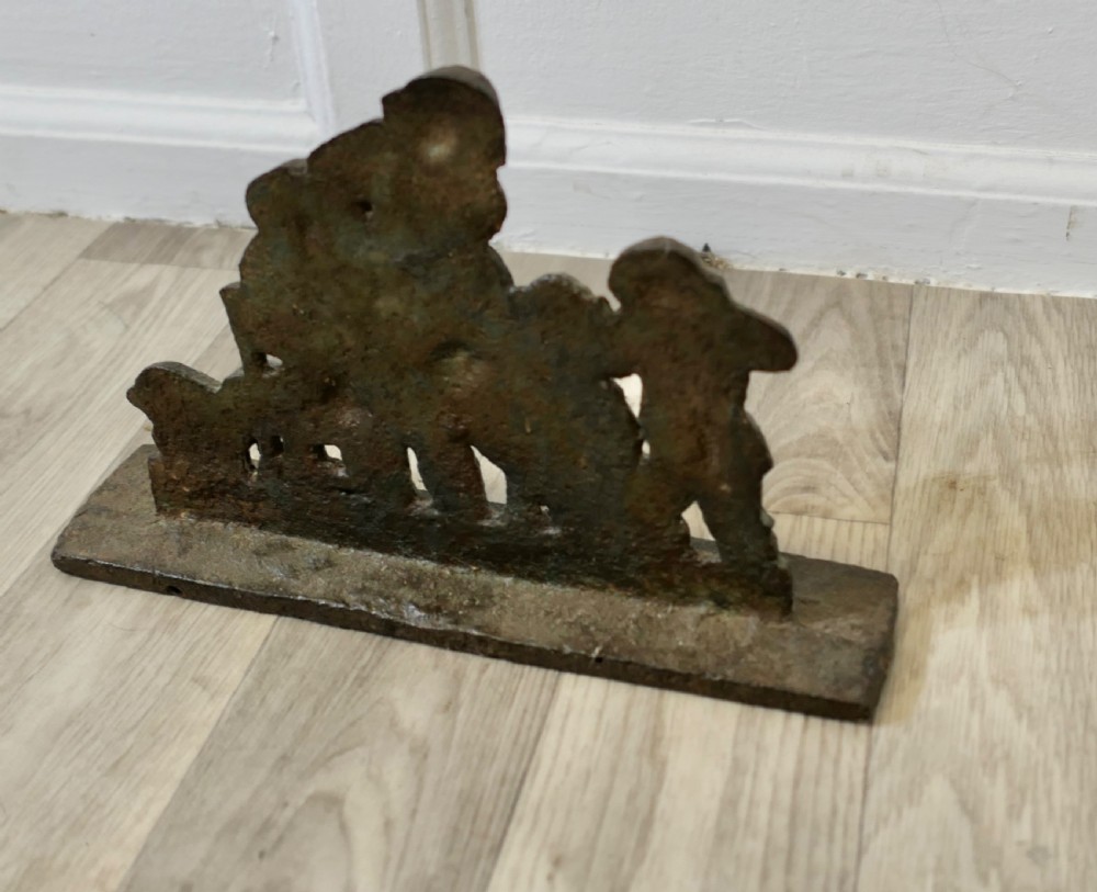 A 19th-century dark cast iron doorstop featuring a figurative narrative scene mounted on a flat rectangular plinth base. View VI