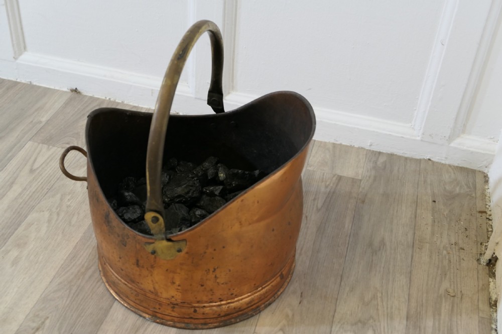 An Arts and Crafts beaten copper helmet coal scuttle featuring a brass overhead swing handle and a small rear tipping handle. View II
