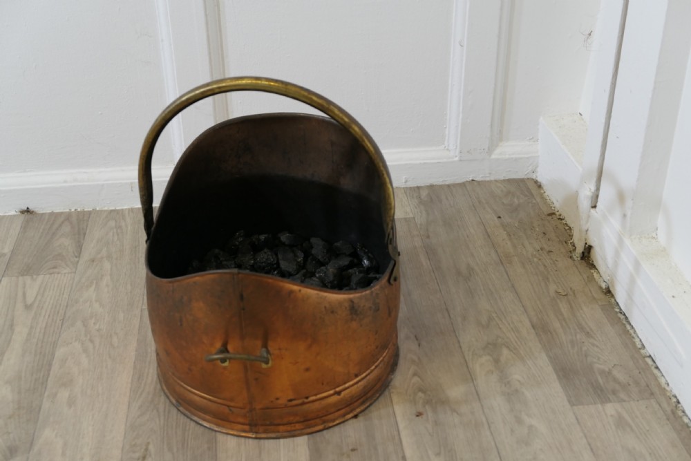 An Arts and Crafts beaten copper helmet coal scuttle featuring a brass overhead swing handle and a small rear tipping handle. View IV