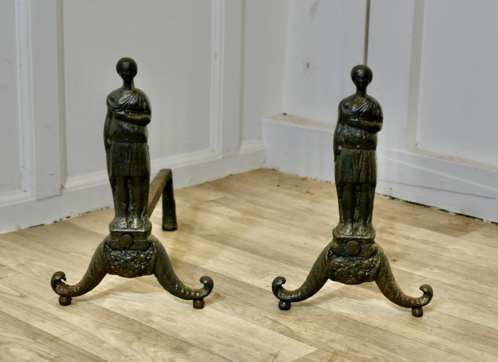 A pair of dark cast iron French Gothic andirons featuring standing guardian figures on scrolled tripod bases.