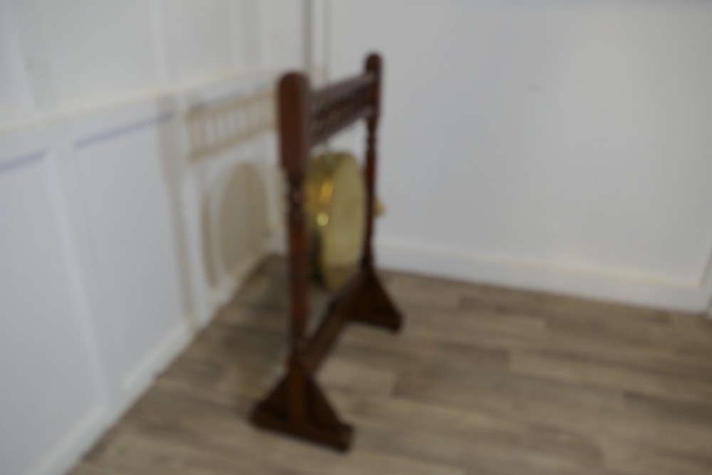 An Arts and Crafts walnut floor-standing dinner gong with turned side columns, a spindle gallery, and a central circular hand-hammered brass disc with attached striker. View III