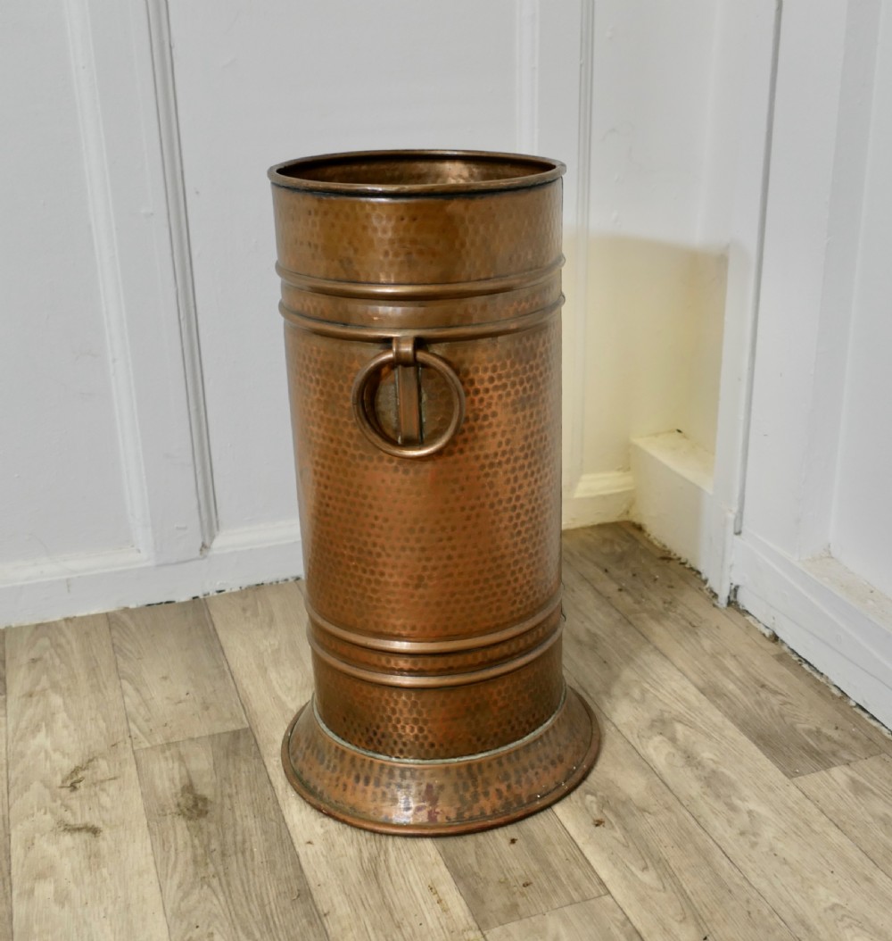 A cylindrical hand-hammered copper umbrella stand featuring raised horizontal ribbing, a flared base, and side ring handles. View II