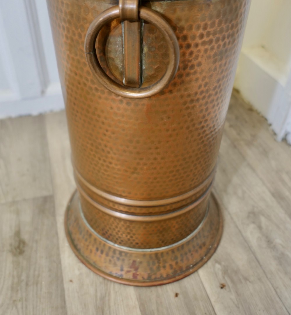 A cylindrical hand-hammered copper umbrella stand featuring raised horizontal ribbing, a flared base, and side ring handles. View III