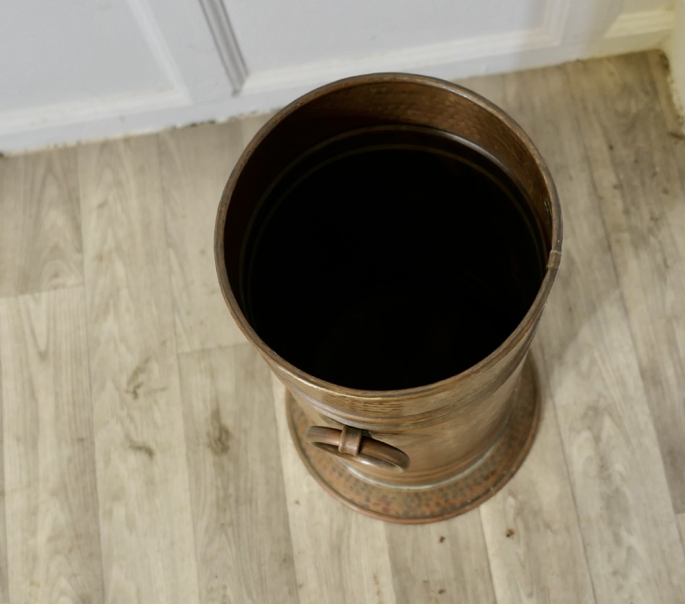 A cylindrical hand-hammered copper umbrella stand featuring raised horizontal ribbing, a flared base, and side ring handles. View IV