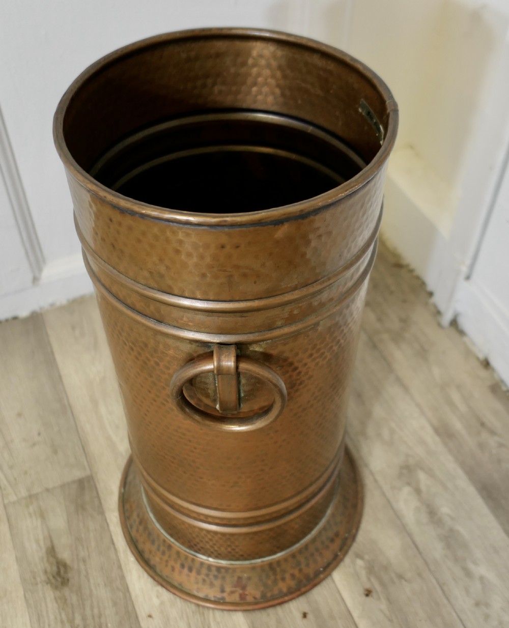 A cylindrical hand-hammered copper umbrella stand featuring raised horizontal ribbing, a flared base, and side ring handles. View VI