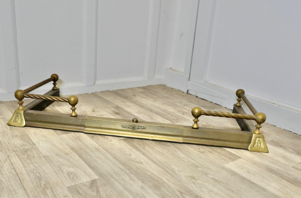 An adjustable Victorian brass fireplace fender featuring barley twist top rails, spherical finials, and central decorative moulding.