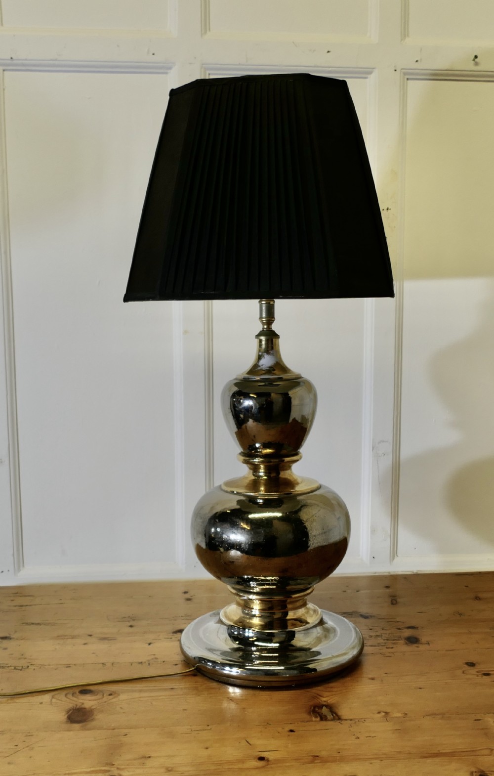 A large Art Deco table lamp featuring a bulbous metallic base in gold and silver finish topped with a black pleated shade.