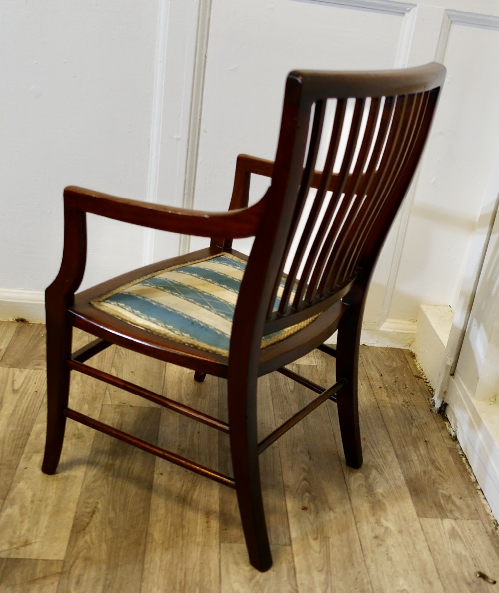 A dark mahogany Regency style childs open armchair with vertical back splats, sweeping armrests, and a striped fabric seat. View III