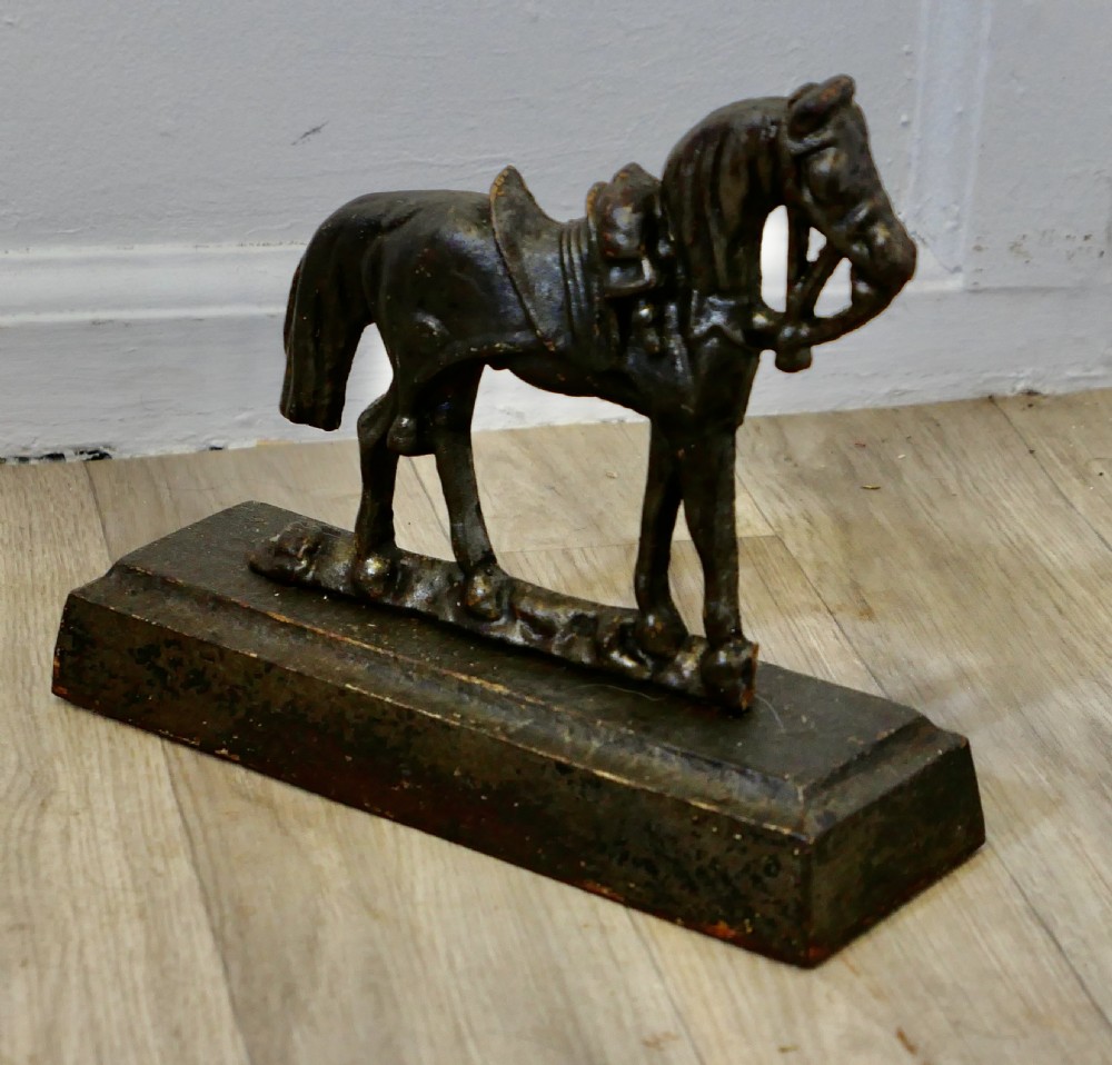 A dark cast iron doorstop featuring a saddled horse standing on a rectangular plinth base. View II