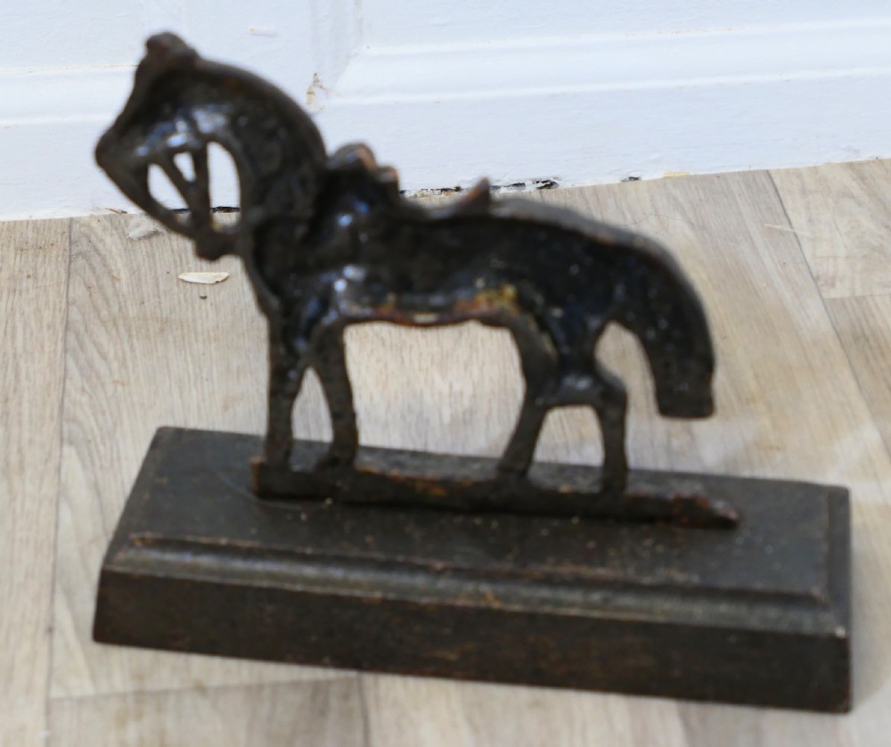 A dark cast iron doorstop featuring a saddled horse standing on a rectangular plinth base. View V