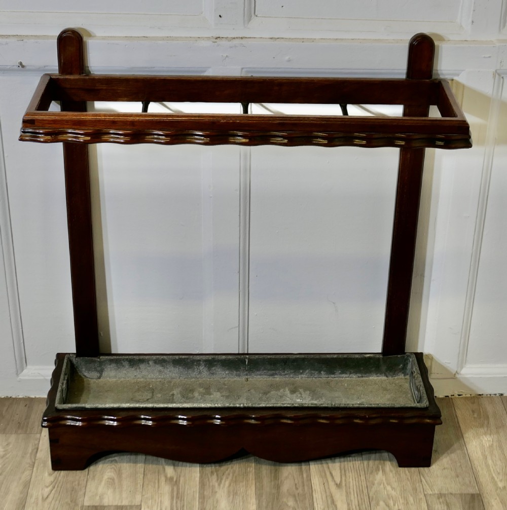 A dark walnut stick stand featuring a upper retention rail with divider bars, scalloped edge moulding, and a metal drip tray inset at the base. View III