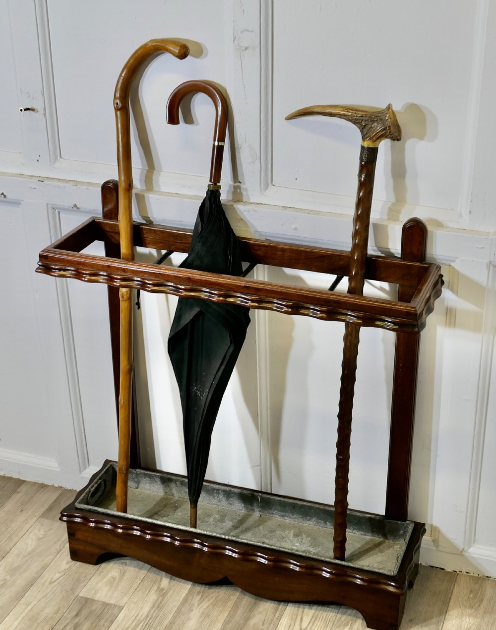 A dark walnut stick stand featuring a upper retention rail with divider bars, scalloped edge moulding, and a metal drip tray inset at the base. View XI