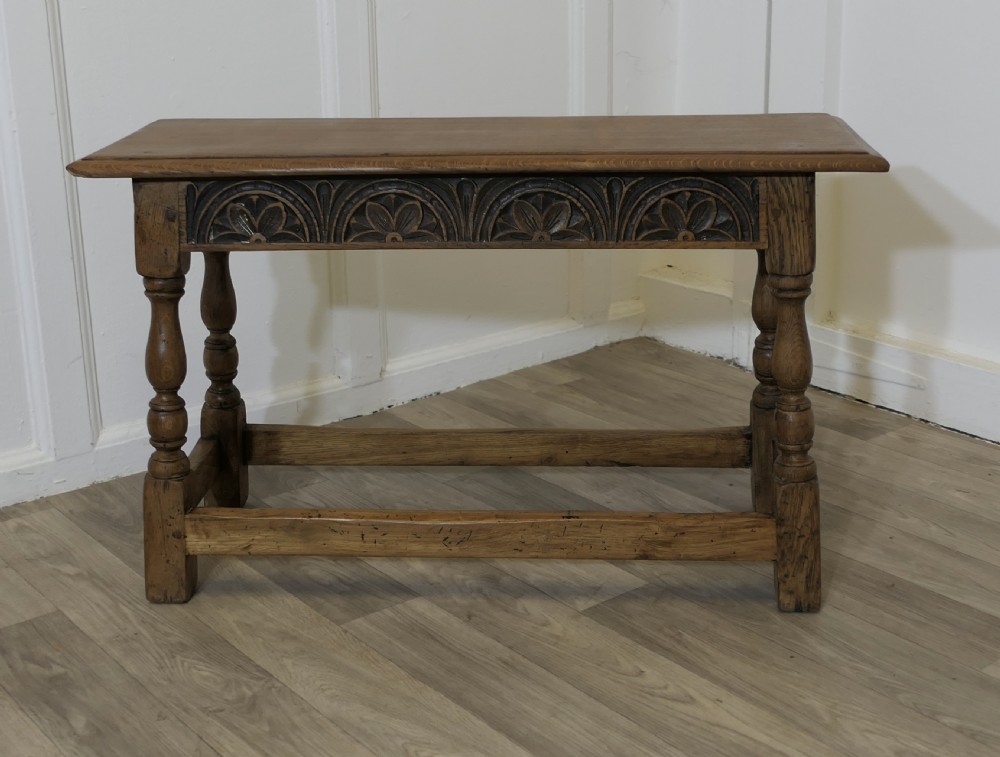 A golden oak joint stool featuring a carved frieze apron, turned legs, and low box stretchers.
