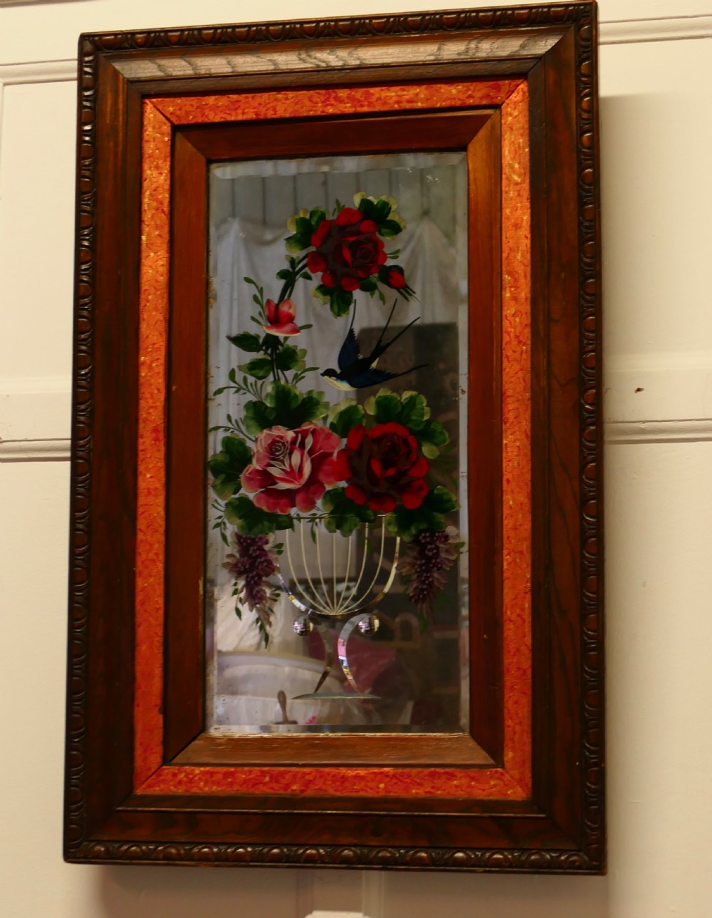 A rectangular Victorian wall mirror featuring a carved wooden frame, a red border, and a central reverse-painted glass panel displaying red roses and a bird in a vase. View V