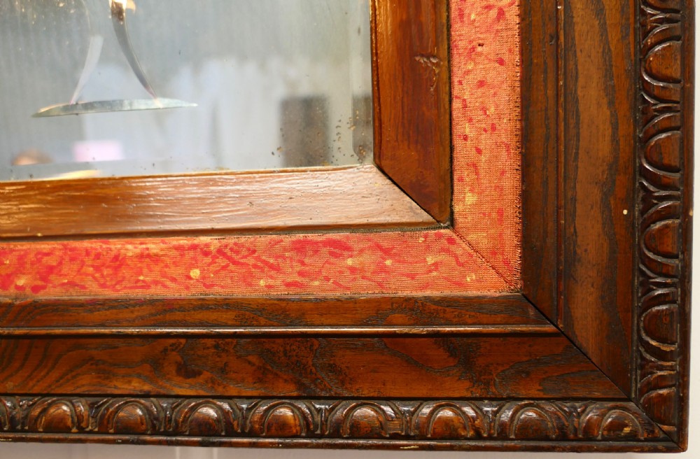 A rectangular Victorian wall mirror featuring a carved wooden frame, a red border, and a central reverse-painted glass panel displaying red roses and a bird in a vase. View VI