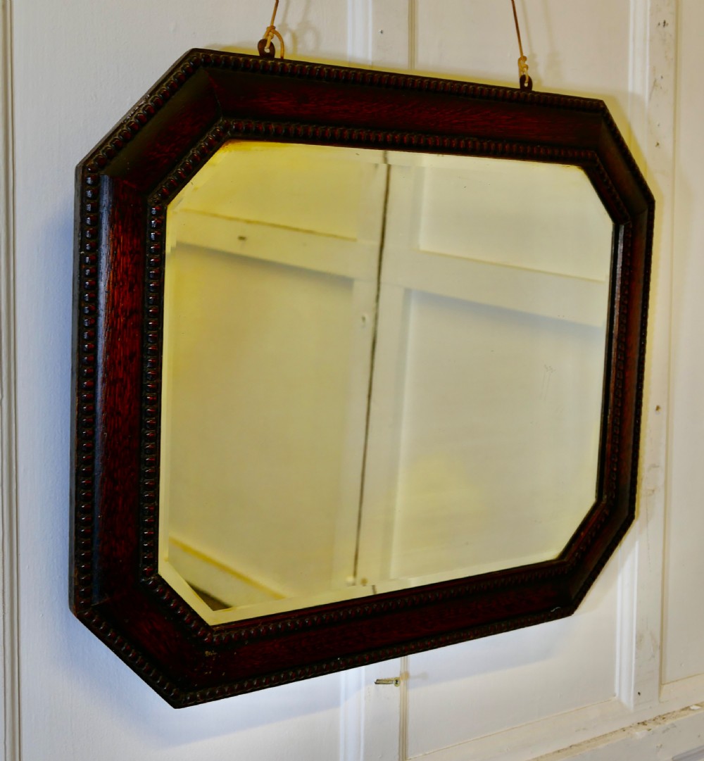 An octagonal dark-stained oak wall mirror featuring beaded moulding along the frame and a bevelled mirror plate.