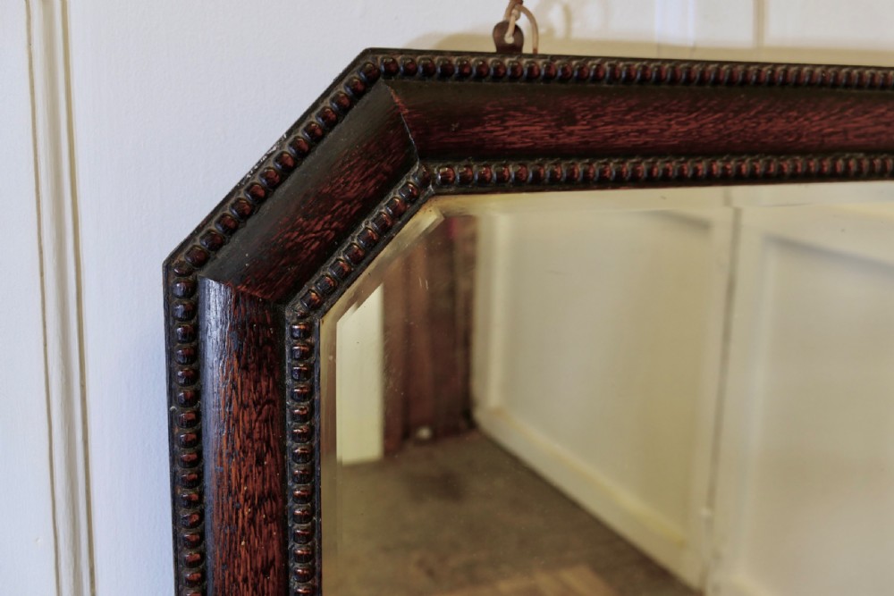 An octagonal dark-stained oak wall mirror featuring beaded moulding along the frame and a bevelled mirror plate. View II