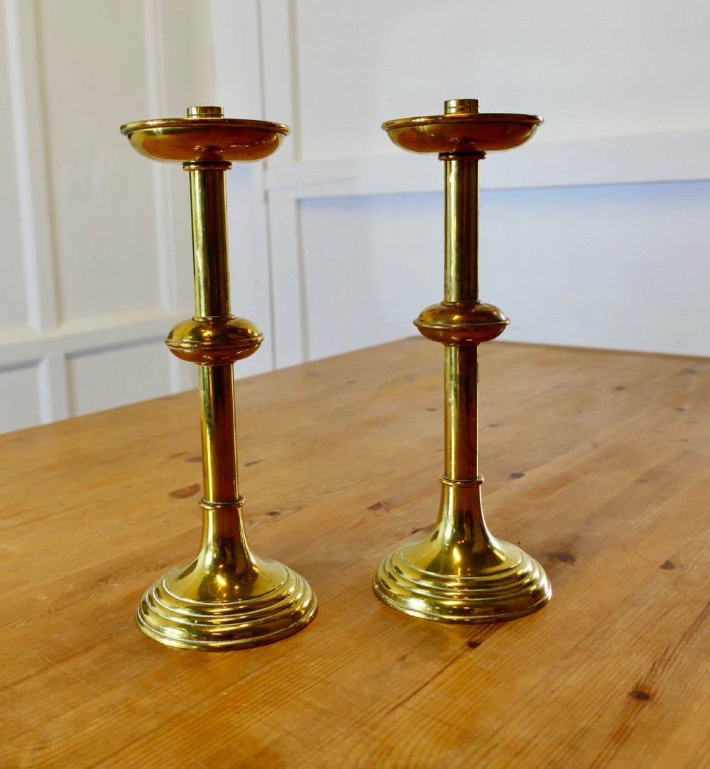 A pair of polished Arts and Crafts brass candlesticks featuring circular stepped bases, central knopped stems, and broad drip pans.