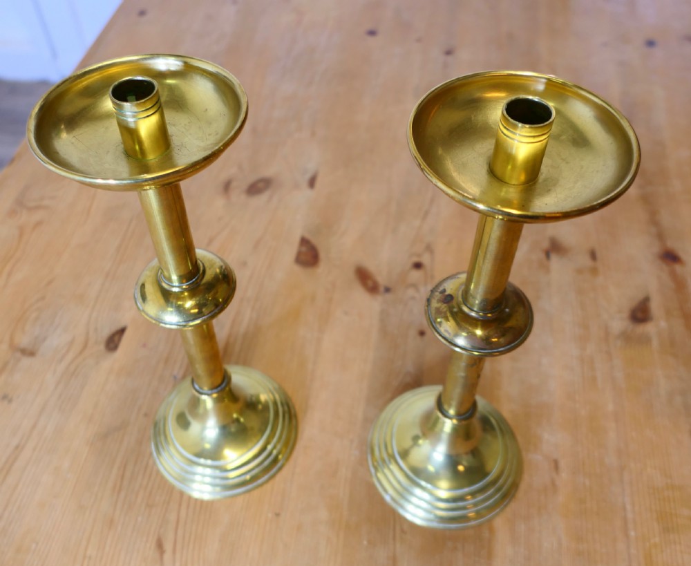 A pair of polished Arts and Crafts brass candlesticks featuring circular stepped bases, central knopped stems, and broad drip pans. View III