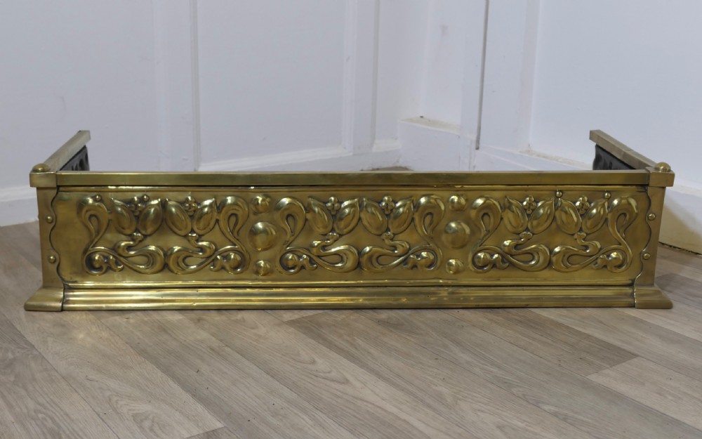 An antique Art Nouveau brass fireplace fender featuring embossed organic floral patterns and corner studs.