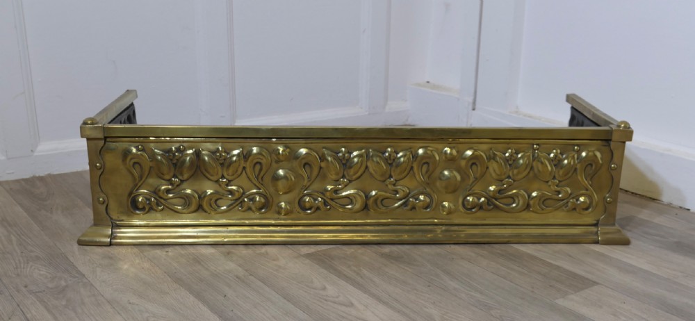 An antique Art Nouveau brass fireplace fender featuring embossed organic floral patterns and corner studs. View II