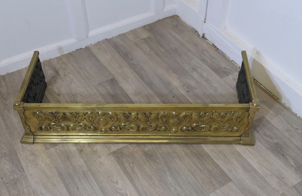 An antique Art Nouveau brass fireplace fender featuring embossed organic floral patterns and corner studs. View III