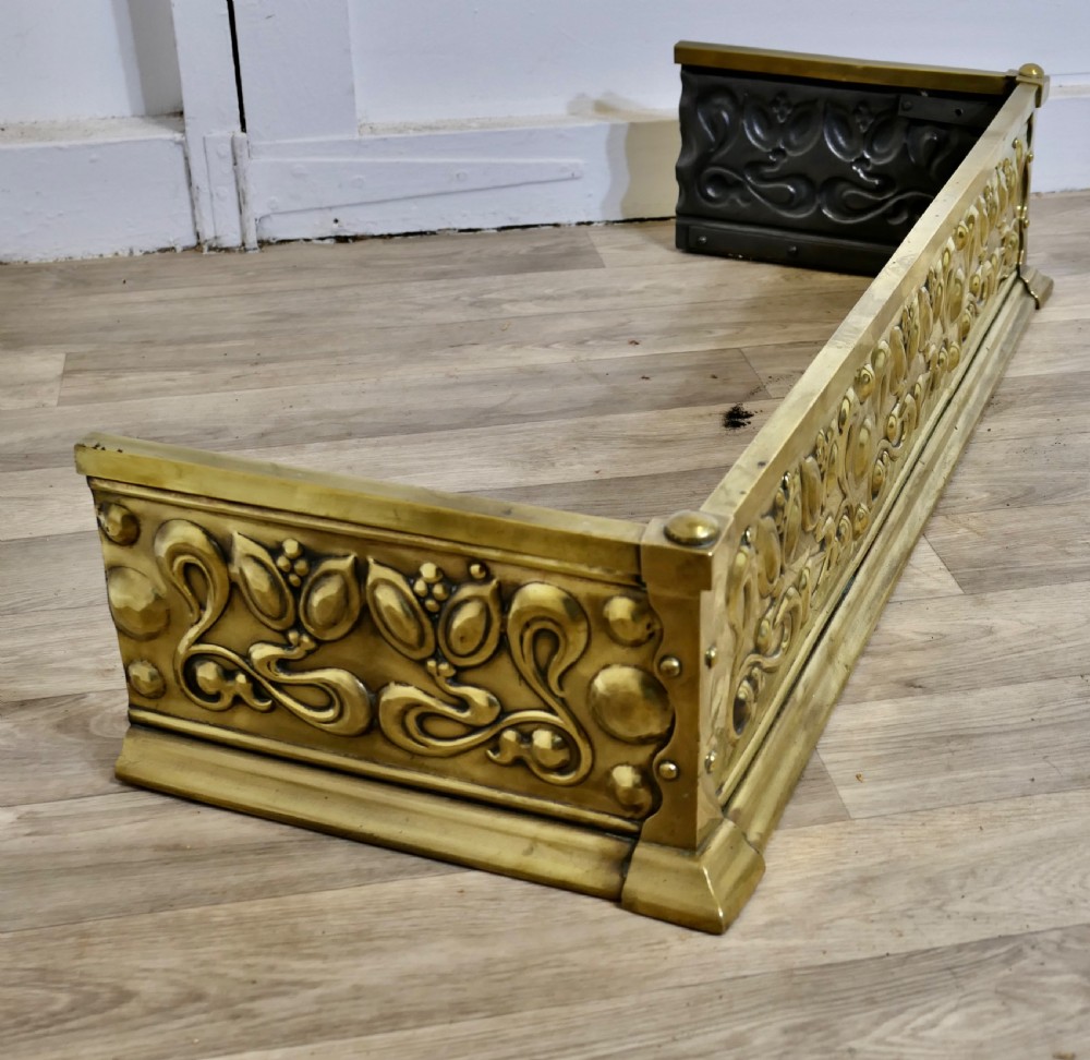 An antique Art Nouveau brass fireplace fender featuring embossed organic floral patterns and corner studs. View IV