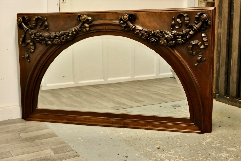 Large rectangular walnut overmantel mirror featuring an arched glass plate decorated with hand-carved floral swags and ribbons.