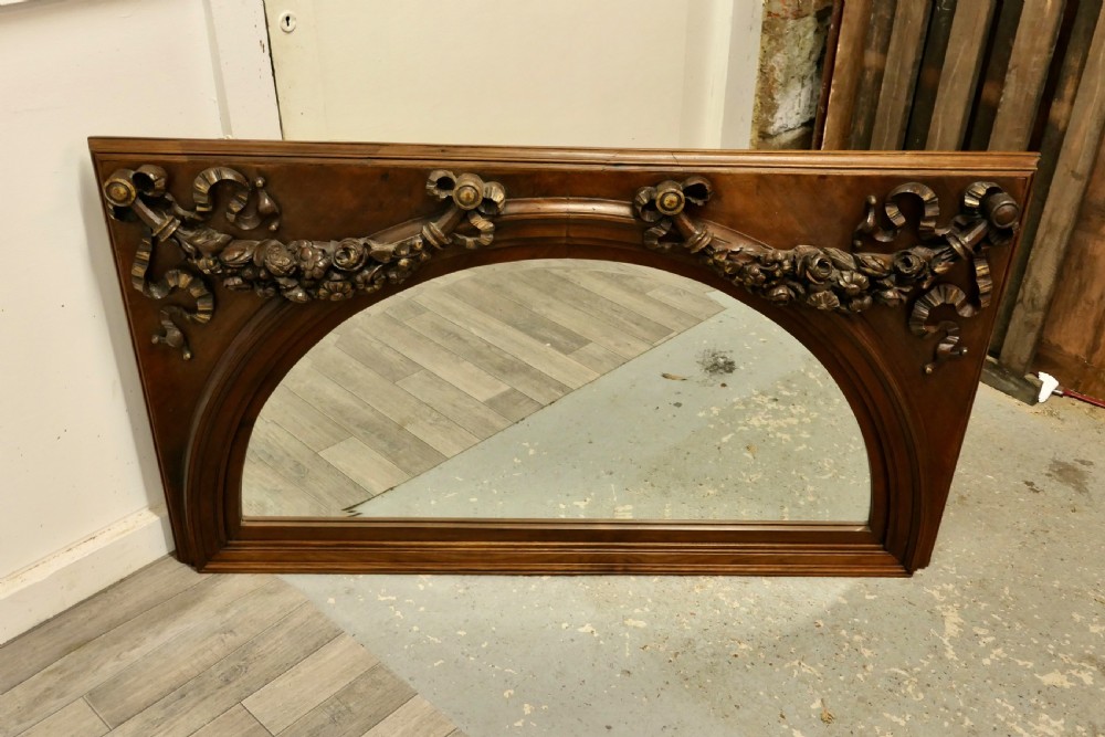 Large rectangular walnut overmantel mirror featuring an arched glass plate decorated with hand-carved floral swags and ribbons. View VII