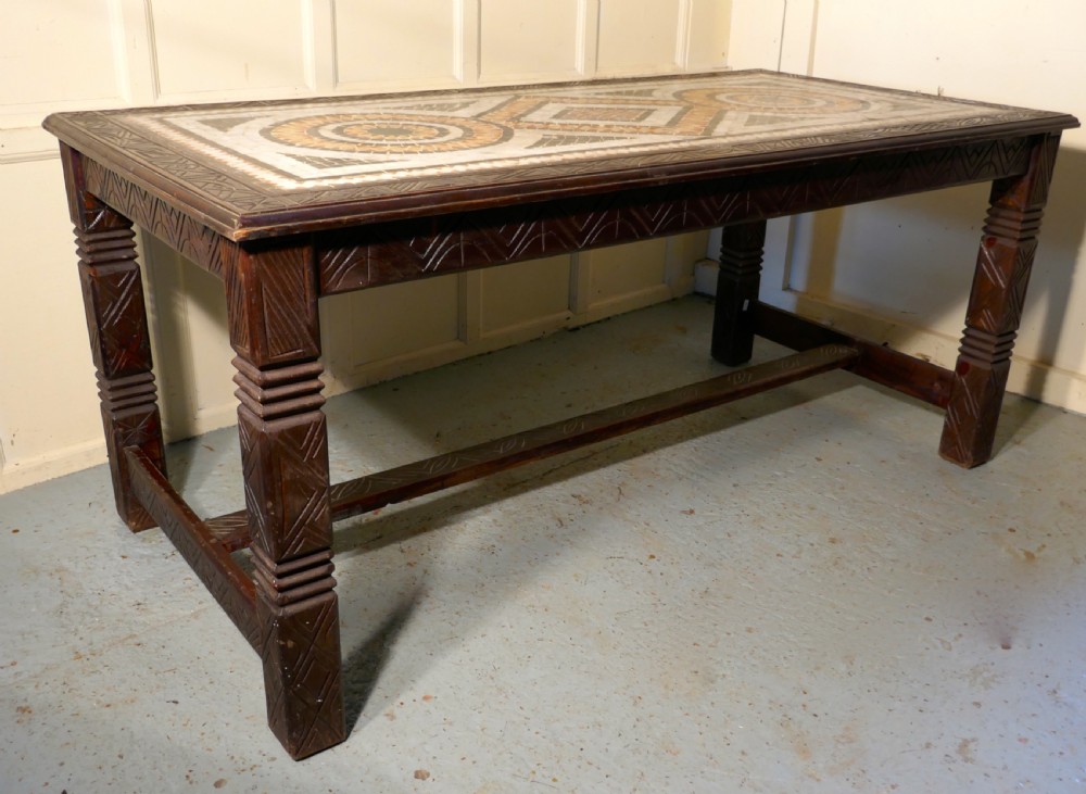 A rectangular dark wood dining table featuring a detailed geometric stone mosaic top, hand-carved geometric patterns on the apron, and carved legs connected by stretchers.